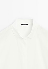 Camicia bianca in cotone con colletto classico, chiusura a bottoni frontale e un'etichetta nera con la scritta "Massimo Dutti" cucita all'interno del colletto.