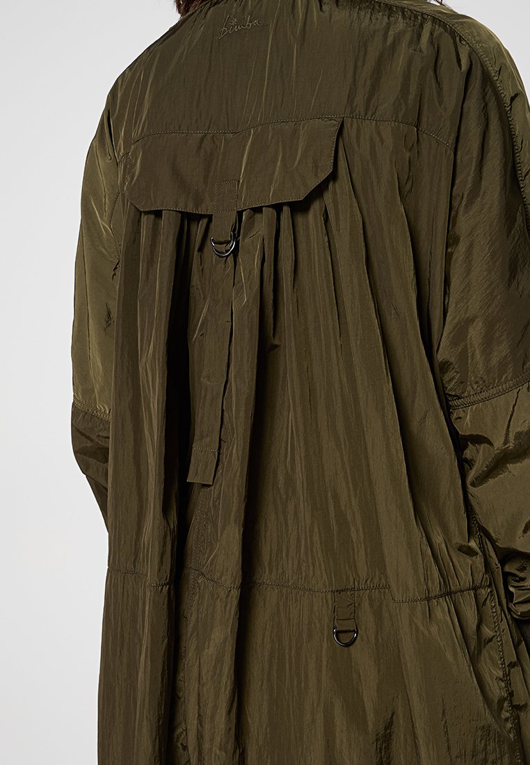Lekka kurtka w oliwkowym kolorze z plisowanym tyłem, zapięciem na napy oraz regulowanym paskiem z metalowym pierścieniem. Wykonana z teksturowanej tkaniny nylonowej.