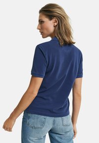 Navyblauwe polo met korte mouwen, kraag en een relaxte fit. Zachte stof met een gladde textuur. De achterkant toont simpele ontwerpelementen.