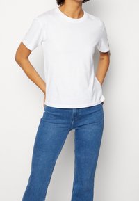 Vit bomullströja med rund hals, korta ärmar och avslappnad passform, kombinerad med blå denimjeans. Enkel och klassisk design.