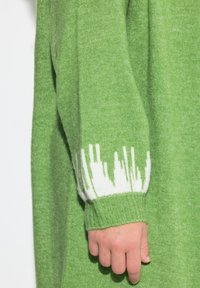 Suéter de punto verde con un puño blanco acanalado con patrones verticales, hecho de material suave, que presenta un color y una textura sólidos.