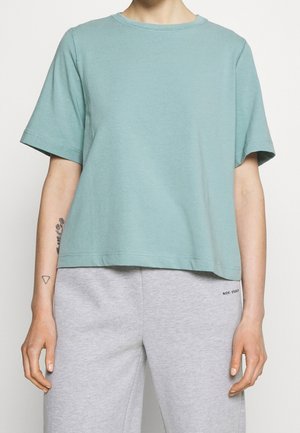 Mint green cotton t-shirt with short sleeves, crew neckline, relaxed fit, and stitching details, worn with gray sweatpants.