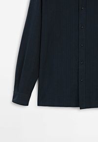 Chemise bleu foncé boutonnée avec des rayures verticales, manches longues et poignets standards, présentant une texture lisse et un col classique.