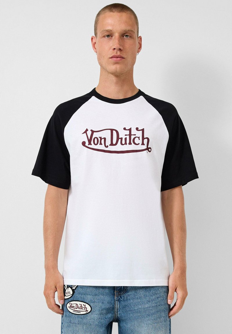 Bijela majica s crnim raglan rukavima, s „Von Dutch“ logotipom u tamnocrvenoj boji preko prsa. Izrađena od mekog pamučnog materijala.