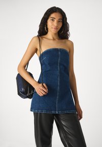 Dunkelblaues, trägerloses Denim-Kleid mit geradem Schnitt, Mittelnaht und rohem Saum; kombiniert mit einer schwarzen, weich strukturierten Umhängetasche.