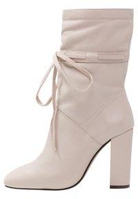 Bottine en cuir beige avec une tige souple, fermeture à lacets et bout pointu sur un talon bloc épais. Texture lisse avec détails de couture.