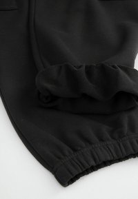 Czarne dresy z miękkiego materiału, elastycznym pasem i ściągaczami na mankietach. Wewnętrzna powierzchnia jest gładka, bez widocznych wzorów.