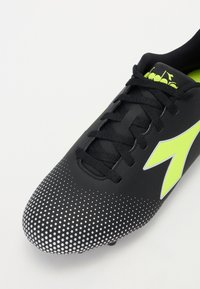 Melnas futbola kurpes ar strukturētu virsmu, neona dzelteniem akcentiem un gradienta rakstu ar baltām punktām. Iekļautas tradicionālas šņorēšanas sistēmas.
