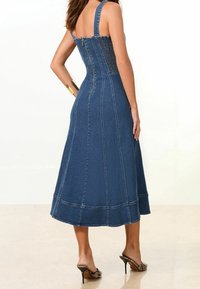 Robe midi en denim avec un bustier ajusté, de larges bretelles, une fermeture éclair à l'arrière et une jupe évasée. Présente des coutures visibles et une surface lisse et texturée.
