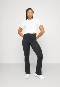 Weißes, kurzes Sportshirt, schwarze, eng anliegende Hose mit seitlichen Akzenten und glatter Textur, kombiniert mit weißen Schuhen. Schlichtes, sportliches Design.