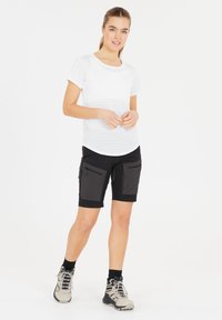 Vit randig t-shirt med rund hals, kombinerad med svarta shorts som har stora framfickor och dragkedjor. Bärs med vandringsskor.