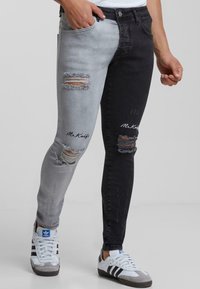 Jeans de denim con un diseño de dos tonos: gris claro en una pierna y gris oscuro en la otra. Presenta desgarros, bordes deshilachados y bordado "Mr. Knuff".