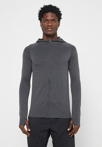 Bluza z kapturem zapinana na zamek w ciemnoszarym kolorze, wykonana z miękkiego materiału z prążkowanymi akcentami i teksturowanymi panelami na ramionach. Długie rękawy z otworami na kciuki.