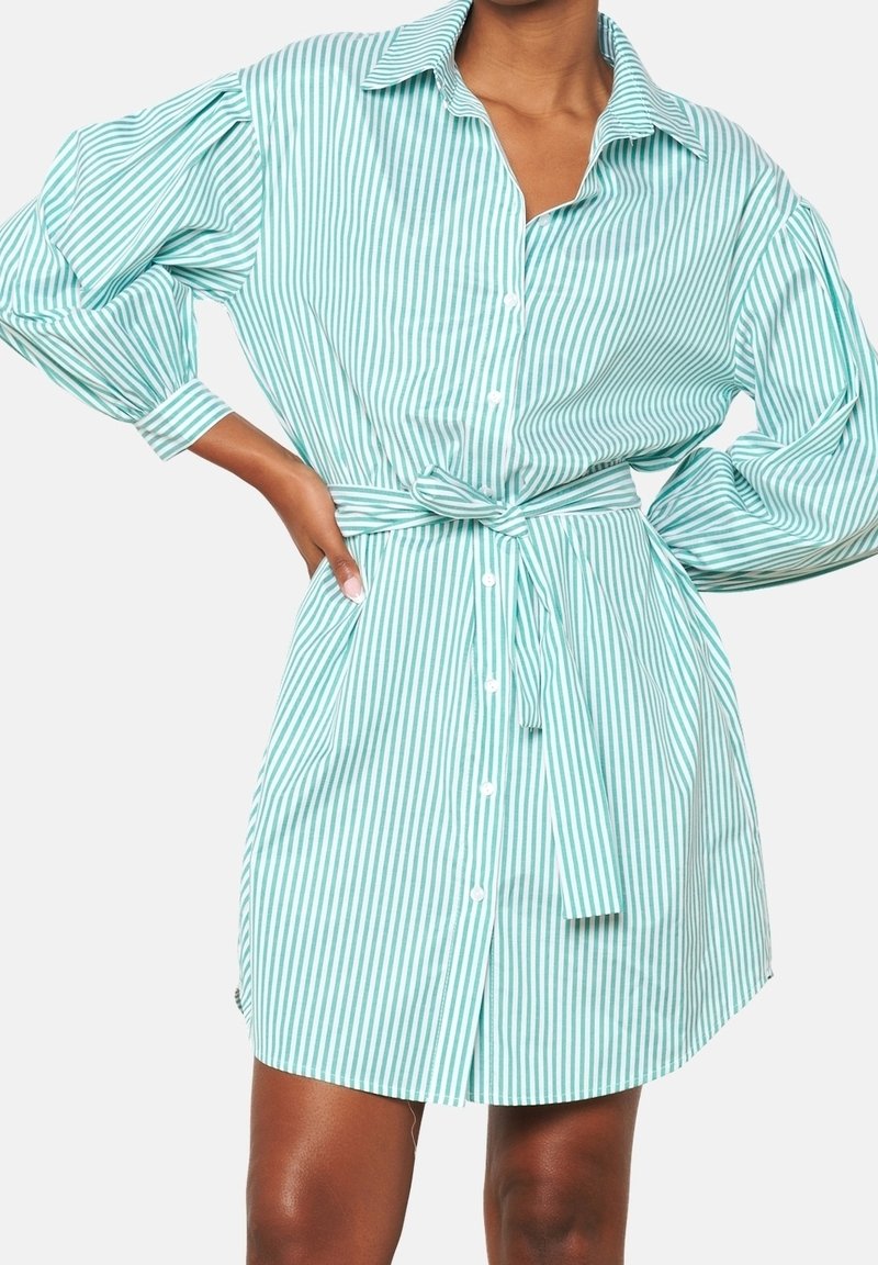 Koszula sukienkowa w jasnym odcieniu teal z białymi paskami, z długimi bufiastymi rękawami oraz przewiązywanym paskiem w talii dla podkreślenia kształtu.