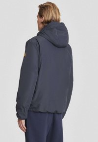 Donkerblauwe hoodie met een soepele textuur en elastische manchetten. Heeft een logo patch op de linkerarm en een relaxte pasvorm.