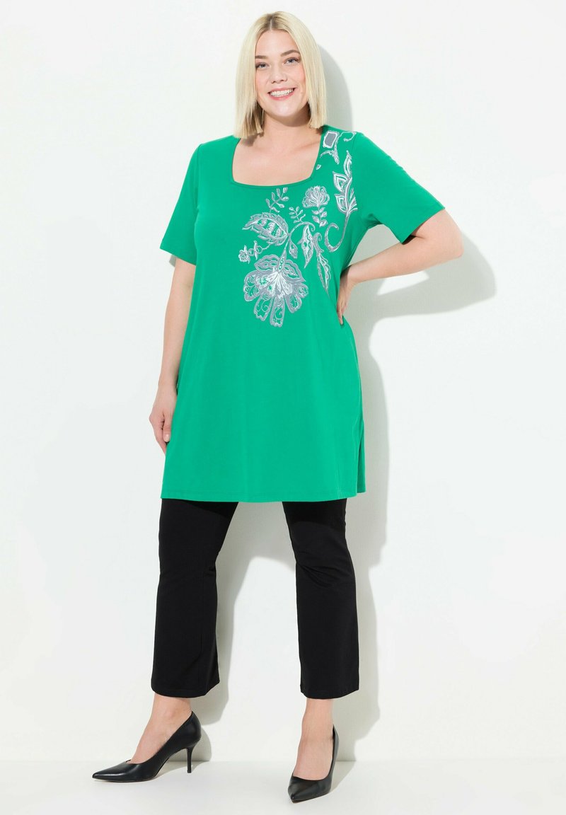 Grøn tunika med kortærmer, firkantet halsudskæring og blomster-sølv broderi på den ene side. Kombineret med sorte cropped bukser og sorte heels.