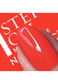 Klart rød neglelakk på en velpleid fingertupp, som viser en blank finish og jevn tekstur mot en uskarp rød bakgrunn.