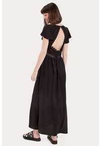 Abito maxi nero con maniche corte a sbuffo, schiena scoperta e dettagli in crochet in vita. Tessuto morbido con una silhouette fluida.