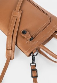 Braune Leder-Umhängetasche mit glatter Textur, verstellbarem Gurt, Reißverschlussfach und schwarzen Hardware-Elementen. Nähte sind an den Kanten sichtbar.