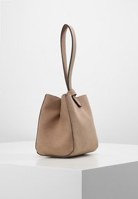 Beige mokkanahkalaukku, jossa on jämäkkä muoto, yksi yläkahva ja hienovaraiset ompeleet reunoilla. Sileä pinta ja minimalistinen muotoilu.