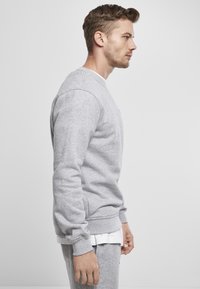 Sudadera gris en mezcla de algodón, con puños y bajo de canalé, un clásico cuello redondo y bolsillos laterales. Lleva debajo una camisa blanca.