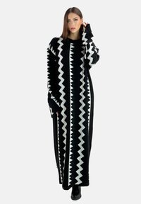 Abito lungo in maglia nera con un motivo a zigzag bianco, maniche ampie e una vestibilità rilassata, adatto per essere indossato a strati o da solo.