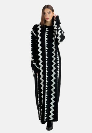 Robe tricotée noire longue avec un motif en zigzag blanc, des manches larges et une coupe ample, idéale pour superposer ou porter seule.