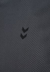 Zwart textiel met een gestructureerd oppervlak, voorzien van kleine perforaties en een verhoogd zwart logo met twee chevron-vormen in het midden.