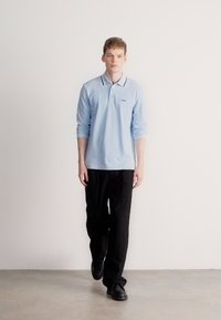 Ανοιχτό μπλε μακρυμάνικο πόλο με μαύρο γιακά, συνδυασμένο με μαύρο παντελόνι και μαύρα παπούτσια. Απλός σχεδιασμός, ομαλή υφή.