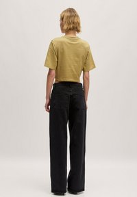 Een cropped olijfgroene t-shirt met korte mouwen, gecombineerd met hoge zwarte wijde jeans met achterzakken en een soepele textuur.
