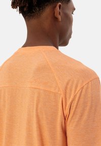 Maglietta sportiva a maniche corte, di colore arancione, realizzata in tessuto testurizzato, con un logo sul retro e design a manica raglan per migliorare il movimento.