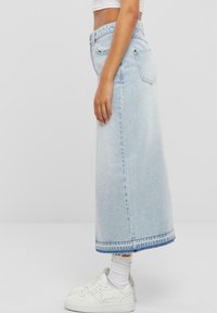 Jupe en denim bleu clair avec une coupe droite, longueur genou et un léger délavage. Elle dispose de poches arrière et d'un ourlet contrasté. Associée à des baskets blanches.