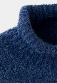Gros plan sur le col roulé en laine épaisse et texturée de couleur bleu foncé.
