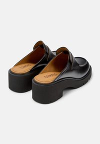 Zoccoli in pelle nera con una robusta suola piatta nera, apertura sul retro e solette color nocciola con il nome del marchio "CAMPER" in rilievo.