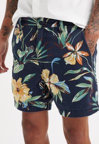 Pantaloni scurți florali din material bleumarin, cu flori mari galbene și portocalii și frunze verzi, având o croială clasică și buzunare laterale.