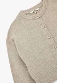 Lichtbeige cardigan van zacht gebreid materiaal. Heeft een ronde halslijn, lange mouwen en drie knopen aan de voorkant. Textuurafwerking.