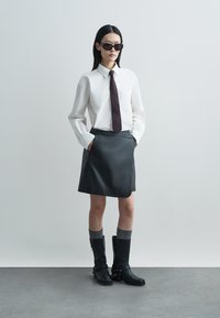 Μαύρη δερμάτινη φούστα, λευκό πουκάμισο με γιακά, μπορντό γραβάτα, μαύρα γυαλιά ηλίου, γκρι πλεκτές κάλτσες και μαύρες μπότες μέχρι το γόνατο με αξεσουάρ από μέταλλο.