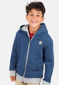 Marineblå zip-up hoodie med gr å indvendig foring, lommer foran og ribbede manchetter. Har et lille logo-patch på brystet.