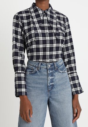 Mujer con camisa de manga larga a cuadros en blanco y negro metida en vaqueros de mezclilla azul claro de cintura alta.