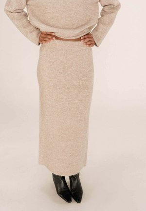 Jupe midi tricotée beige en tissu doux et texturé, avec une silhouette droite, associée à des bottines noires à bout pointu.