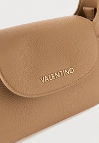 Brązowa skórzana torebka z teksturowaną powierzchnią, z logo "VALENTINO" w kolorze złotym na klapie. Zaokrąglony kształt z magnetycznym zapięciem.