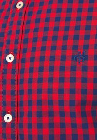 Chemise à carreaux rouge et bleu marine avec boutons blancs et petites lettres brodées sur la poitrine.