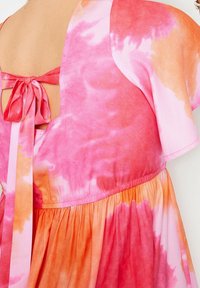 Bavlněné šaty s tie-dye vzorem v růžových a oranžových odstínech, se zadním otvorem ve tvaru klíče a širokými volánovými rukávy. Měkká textura.