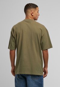 Olivengrøn bomulds t-shirt med korte ærmer, afslappet pasform og rund halsudskæring. Bagfra ses en sømløs design uden synlig branding.