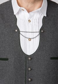 Grau gestrickte Weste mit grünen Akzenten, silbernen Knöpfen und einer Kettenverzierung über einem weißen, plissierten Kragen.