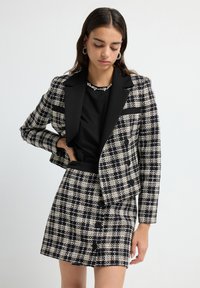 Blazer a scacchi bianco e nero con revers neri e gonna corta abbinata. Tessuto testurizzato con bottoni in evidenza e vestibilità strutturata.