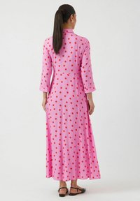 Lang rosa kjole med røde prikker, med krage, trekvart ermer og en flytende silhuett. Glatt stoff med en avslappet passform.