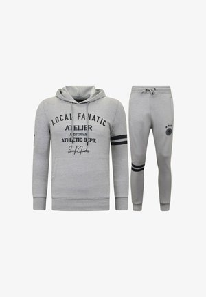 Grijze hoodie met zwarte tekst en strepen, voorzien van een voorvak. Bijpassende grijze joggingbroek met strepen en een logopatch op het bovenbeen.