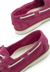 Rosa Wildlederschlappen mit weißen Nähten und silbernen Ösen. Sie verfügen über eine gepolsterte Innensohle mit Perforationen und eine Gummisohle.