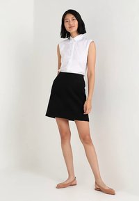 White sleeveless blouse with a collar paired with a black A-line skirt. Model wears nude flats. Clean lines, casual fit, and neutral colors.